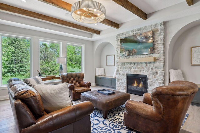 living room with beam ceiling, an inviting chandelier, light hardwood / wood-style floors, and a stone fireplace