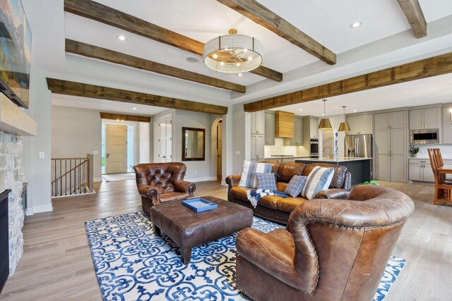 living room with sink, beam ceiling, a stone fireplace, and light wood-type flooring