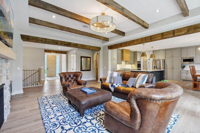 living room featuring a stone fireplace, beamed ceiling, light wood-style flooring, and baseboards