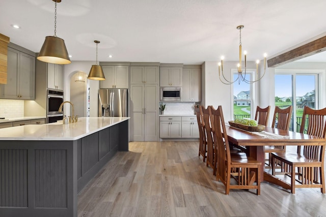 kitchen with a large island, gray cabinets, hanging light fixtures, light wood-style flooring, and appliances with stainless steel finishes