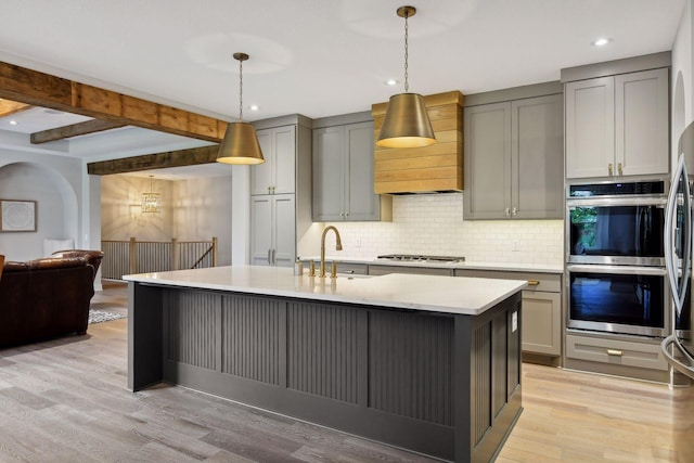 kitchen featuring double oven, beamed ceiling, light hardwood / wood-style floors, tasteful backsplash, and hanging light fixtures