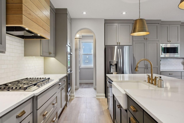 kitchen featuring light wood-type flooring, backsplash, gray cabinets, custom range hood, and appliances with stainless steel finishes