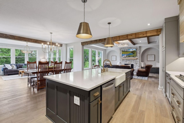 kitchen with beam ceiling, dishwasher, a center island with sink, light wood-type flooring, and a stone fireplace