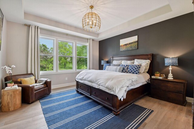 bedroom with a notable chandelier, a raised ceiling, and light wood-type flooring