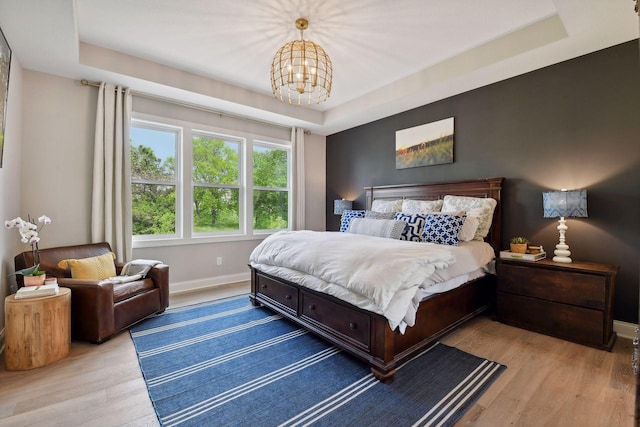 bedroom with light wood finished floors, baseboards, a raised ceiling, and an inviting chandelier