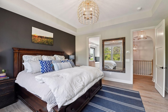 bedroom with hardwood / wood-style flooring, a notable chandelier, and a tray ceiling