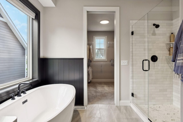 bathroom featuring a stall shower, wainscoting, a soaking tub, tile patterned floors, and a spacious closet