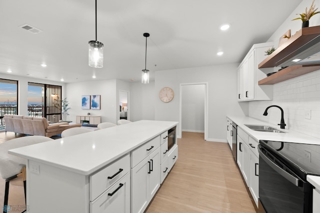 kitchen featuring sink, white cabinetry, hanging light fixtures, black appliances, and wall chimney exhaust hood