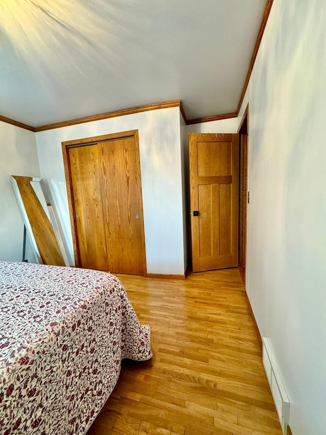 bedroom featuring baseboard heating, ornamental molding, light hardwood / wood-style floors, and a closet