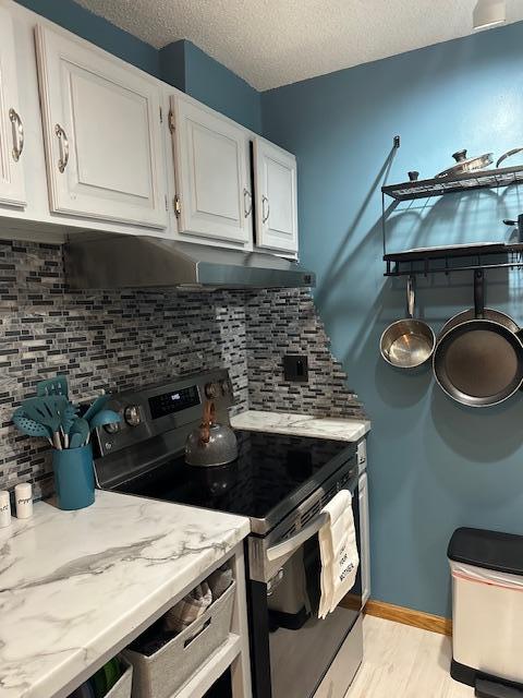 kitchen with stainless steel range with electric stovetop, light stone counters, white cabinetry, and decorative backsplash