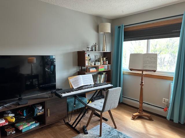 office area with baseboard heating, light hardwood / wood-style flooring, and a textured ceiling