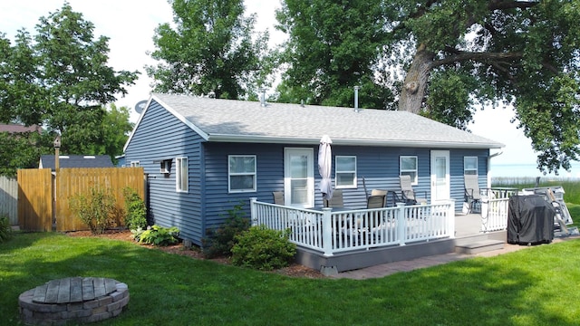 back of property featuring a yard, a shingled roof, fence, a deck, and a fire pit