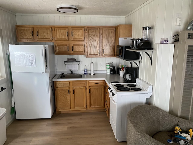 kitchen featuring white appliances, brown cabinetry, light countertops, light wood-style floors, and a sink