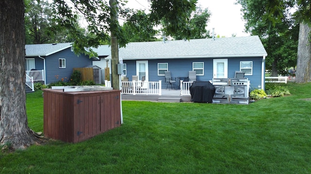 back of property with a deck, roof with shingles, a yard, and a hot tub