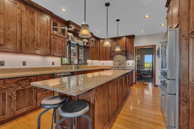 kitchen featuring a kitchen island, glass insert cabinets, a kitchen breakfast bar, decorative light fixtures, and stainless steel appliances