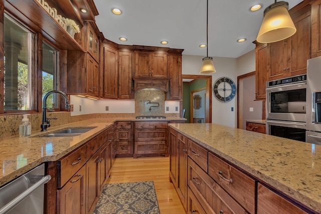 kitchen with pendant lighting, stainless steel appliances, glass insert cabinets, a sink, and light stone countertops