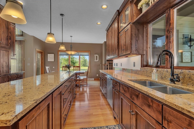 kitchen featuring light wood finished floors, dishwasher, decorative light fixtures, light stone countertops, and a sink