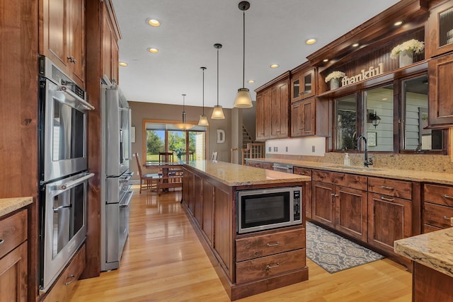 kitchen with light stone counters, appliances with stainless steel finishes, glass insert cabinets, a sink, and a kitchen island