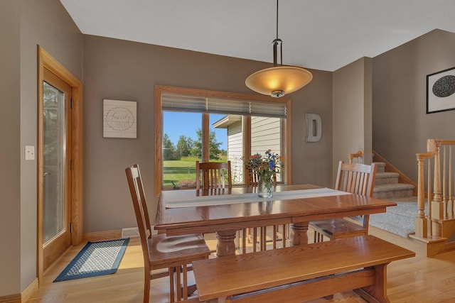 dining space with light wood-style flooring, baseboards, and stairs