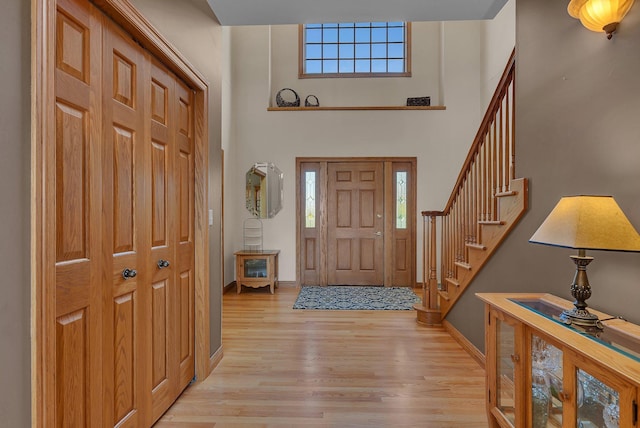 entrance foyer with light wood-type flooring, plenty of natural light, stairs, and a towering ceiling