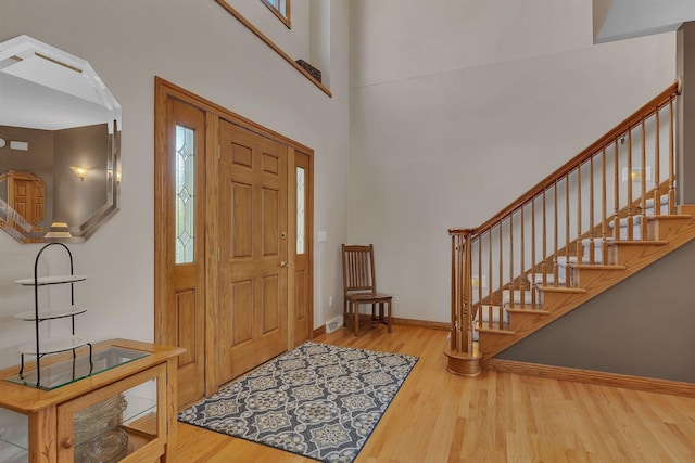 foyer with a towering ceiling, stairs, baseboards, and wood finished floors