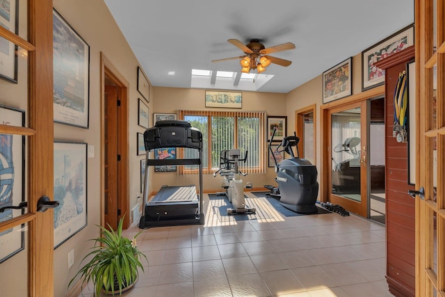 workout area with ceiling fan, light tile patterned floors, and a skylight