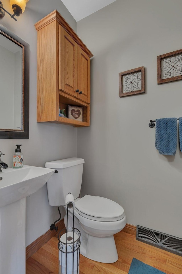 half bath with toilet, baseboards, visible vents, and wood finished floors