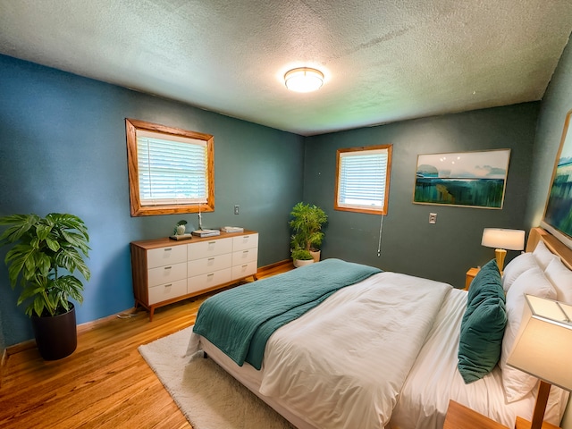 bedroom featuring light hardwood / wood-style floors, multiple windows, and a textured ceiling