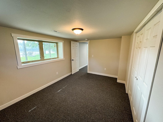 unfurnished bedroom featuring a textured ceiling, a closet, and dark carpet