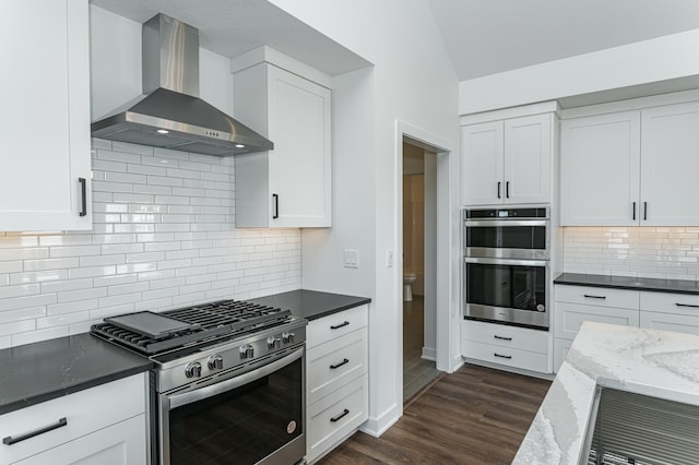 kitchen featuring dark hardwood / wood-style floors, stainless steel appliances, white cabinets, decorative backsplash, and wall chimney exhaust hood