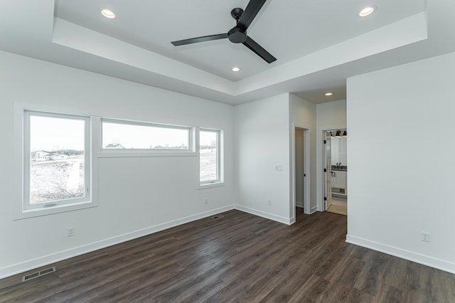 spare room with a tray ceiling, dark wood-type flooring, and ceiling fan