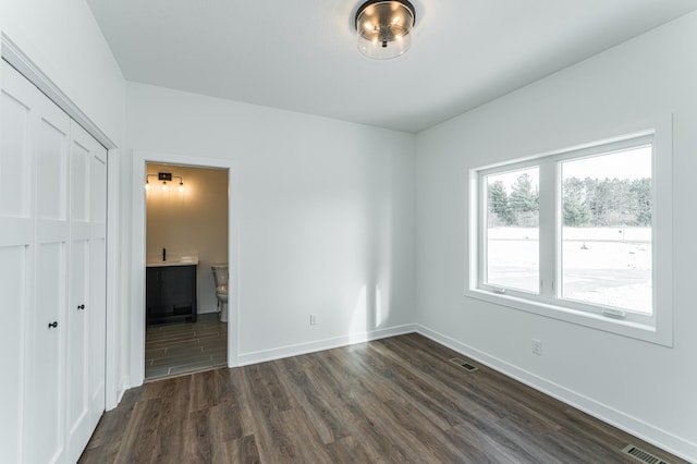 unfurnished bedroom featuring ensuite bathroom, dark hardwood / wood-style flooring, and a closet