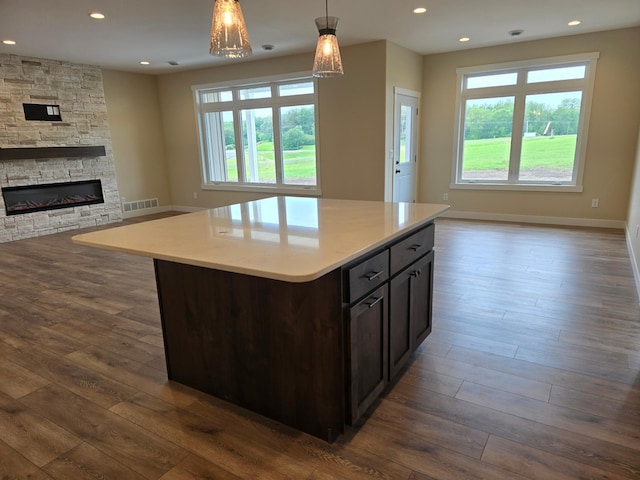 kitchen with a center island, a stone fireplace, dark hardwood / wood-style flooring, and decorative light fixtures