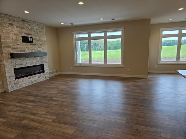 unfurnished living room with dark wood-type flooring and a stone fireplace