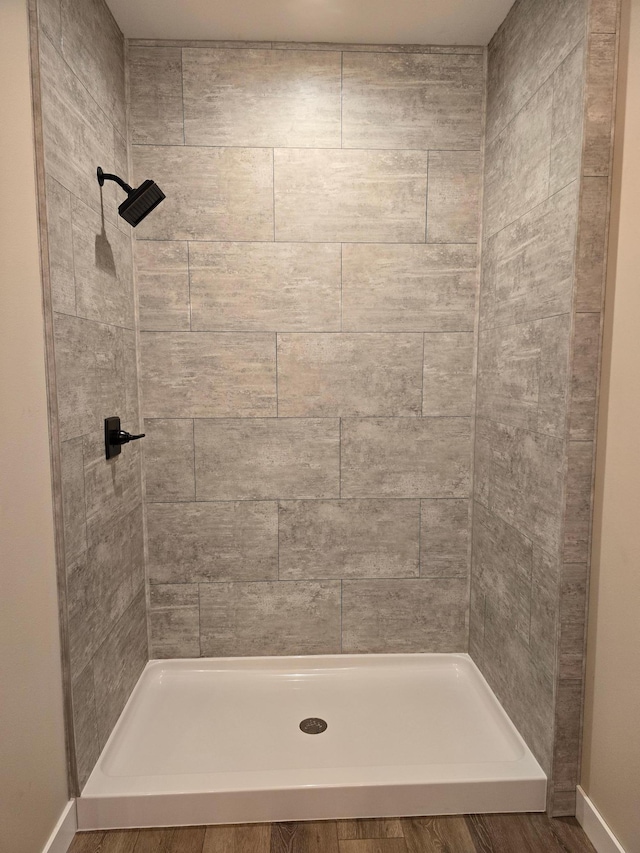 bathroom with a tile shower and wood-type flooring