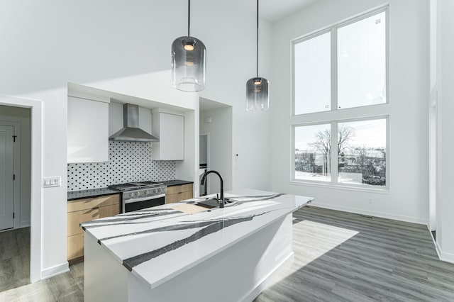 kitchen with dark wood-type flooring, backsplash, decorative light fixtures, stainless steel gas stove, and wall chimney range hood