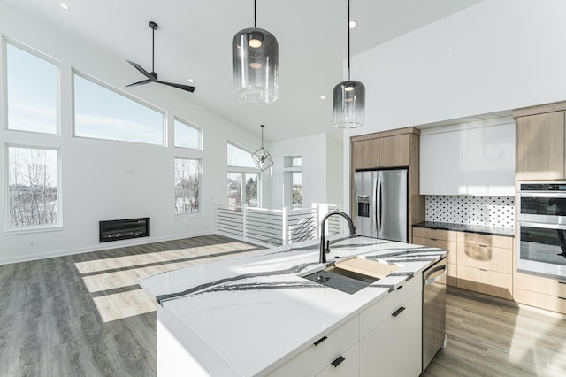 kitchen with appliances with stainless steel finishes, decorative backsplash, a center island with sink, and light hardwood / wood-style floors