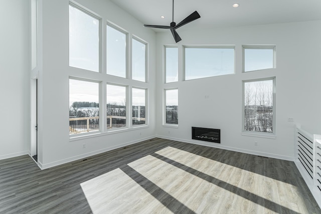 unfurnished living room featuring ceiling fan, dark wood-type flooring, and a high ceiling