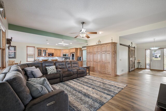 living area with baseboards, a barn door, wood finished floors, a textured ceiling, and a ceiling fan