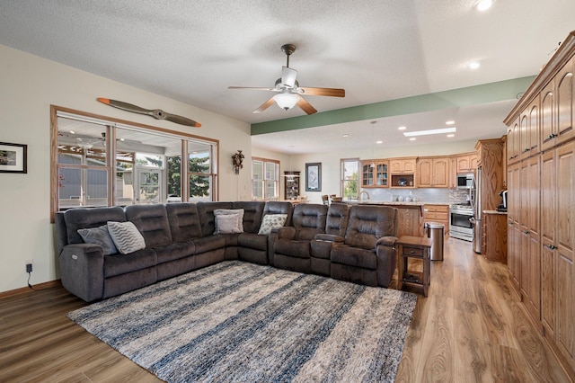 living area featuring light wood-style flooring, a textured ceiling, and ceiling fan