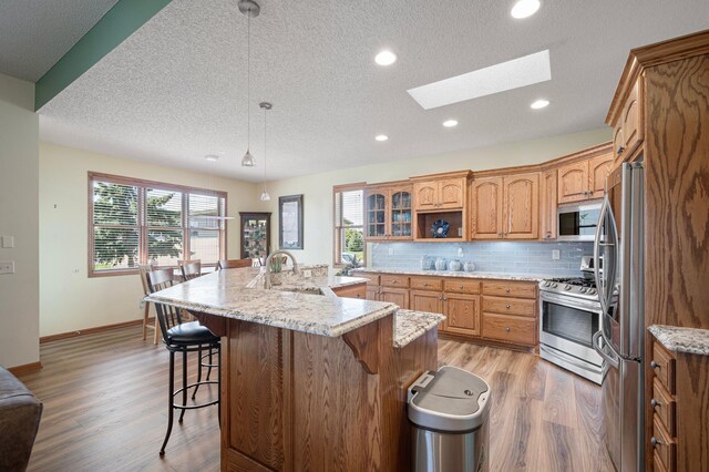 kitchen featuring a skylight, a sink, stainless steel appliances, a kitchen bar, and backsplash