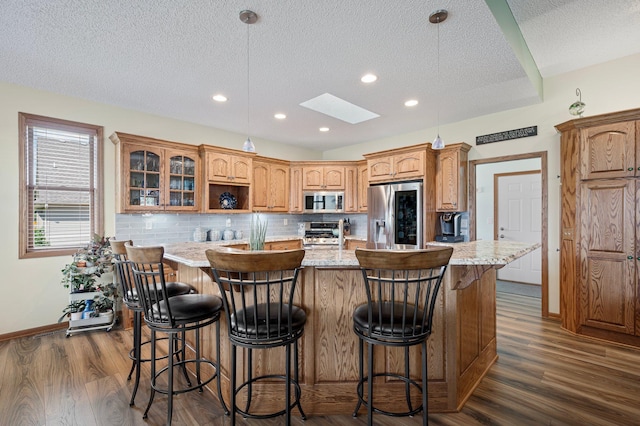 kitchen with a skylight, an island with sink, dark wood-style flooring, and stainless steel appliances