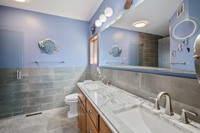 bathroom featuring tile walls, tiled shower, visible vents, and a sink