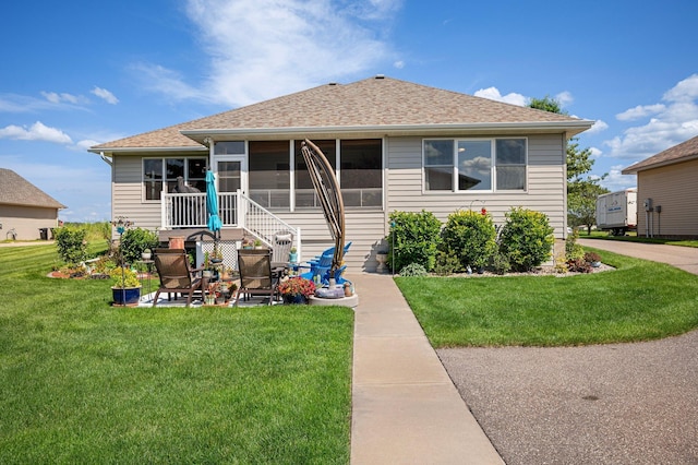 rear view of house with a patio area, a shingled roof, a yard, and a sunroom