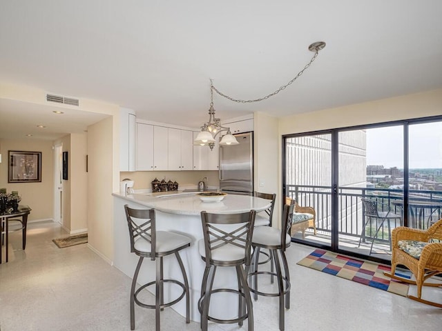 kitchen with pendant lighting, white cabinets, kitchen peninsula, stainless steel refrigerator, and a chandelier