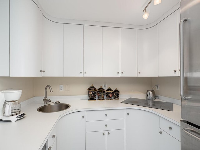 kitchen with stainless steel fridge, white cabinetry, and sink