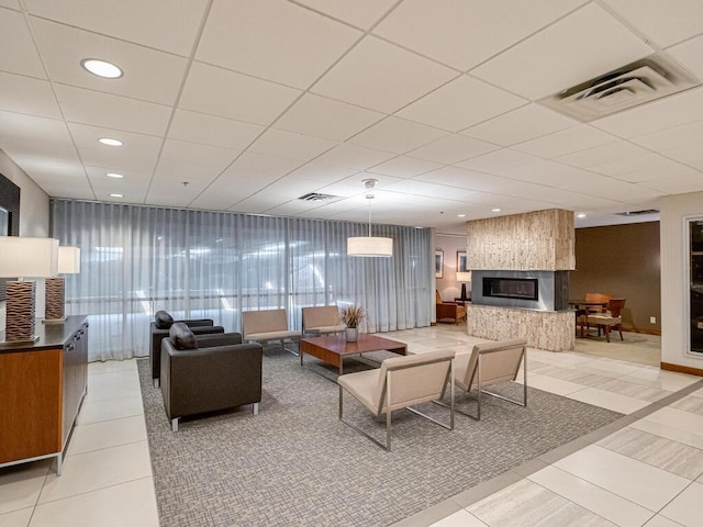 tiled living room featuring a large fireplace and a drop ceiling