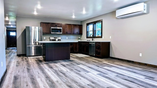 kitchen featuring dark brown cabinetry, a wall mounted AC, a kitchen island, light hardwood / wood-style flooring, and stainless steel appliances