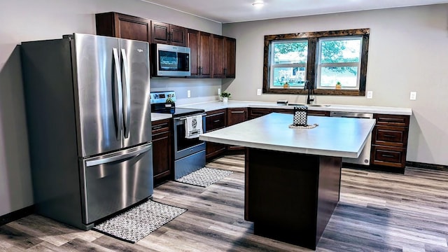 kitchen featuring sink, a kitchen island, dark brown cabinets, stainless steel appliances, and light wood-type flooring