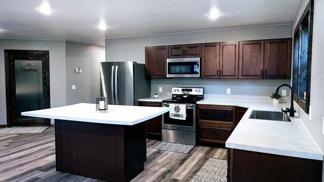 kitchen with a breakfast bar area, stainless steel appliances, a center island, hardwood / wood-style flooring, and sink